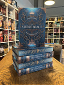 Das Bild zeigt einen Stapel von "Die vierte Braut". Das Cover ist dabei direkt auf den Betrachter gerichtet und der Farbschnitt sowie der Buchrücken bei den liegenden Büchern sichtbar.