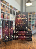 Das Bild zeigt einen Stapel von "Red Raven Castle". Das Cover ist dabei direkt auf den Betrachter gerichtet und der Farbschnitt sowie der Buchrücken bei den liegenden Büchern sichtbar.