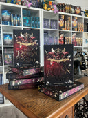 Das Bild zeigt einen Stapel von "Red Raven Castle". Das Cover ist dabei direkt auf den Betrachter gerichtet und der Farbschnitt sowie der Buchrücken bei den liegenden Büchern sichtbar.