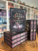 Das Bild zeigt einen Stapel von "Jack the Ripper's Sammlung der Herzen". Das Cover ist dabei direkt auf den Betrachter gerichtet und der Farbschnitt sowie der Buchrücken bei den liegenden Büchern sichtbar.
