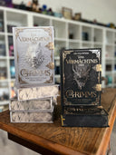 Das Bild zeigt zwei Stapel von "Das Vermächtnis der Grimms"; den Band 1 in Weiß und Band 2 in Schwarz. Das Cover ist dabei direkt auf den Betrachter gerichtet und der Farbschnitt sowie der Buchrücken bei den liegenden Büchern sichtbar.