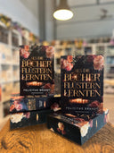 Das Bild zeigt einen Stapel von "Als die Bücher flüstern lernten". Das Cover ist dabei direkt auf den Betrachter gerichtet und der Farbschnitt sowie der Buchrücken bei den liegenden Büchern sichtbar.