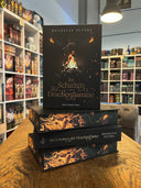 Das Bild zeigt einen Stapel von "Im Schatten der Drachenflamme". Das Cover ist dabei direkt auf den Betrachter gerichtet und der Farbschnitt sowie der Buchrücken bei den liegenden Büchern sichtbar.