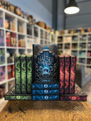 Das Bild zeigt drei Stapel von "Die 12 Häuser der Magie" - Band 1 bis 3 in Blau, Rot und Grün. Das Cover ist dabei direkt auf den Betrachter gerichtet und der Farbschnitt sowie der Buchrücken bei den liegenden Büchern sichtbar.