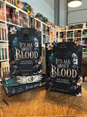 Das Bild zeigt einen Stapel von "It's all about blood". Das Cover ist dabei direkt auf den Betrachter gerichtet und der Farbschnitt sowie der Buchrücken bei den liegenden Büchern sichtbar.