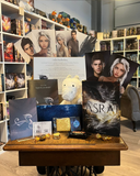 Das Produktbild zeigt den Inhalt des Asrai-Starter-Sets: Oben die Page Overlays der Hauptfiguren, mittig die Plüsch-Manila, daneben die Schmuckausgabe des ersten Bandes und drumherum die anderen Goodies - die Kurzgeschichte, die Visitenkarte, den Drachenmond-Keks, den Brief, die Charakterkarten und ein paar Süßigkeiten.