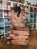 Das Bild zeigt einen Stapel von "Ein Kater für zwei Herzen". Das Cover ist dabei direkt auf den Betrachter gerichtet und der Farbschnitt sowie der Buchrücken bei den liegenden Büchern sichtbar.