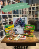 Das Produktbild zeigt den Inhalt der Drachenpost "Blind Date with a Book". Neben dem frei wählbaren Buch, das in ein Drachenposter eingepackt wird, erhält man eine Buchstabensuppe, Gummibärchen, einen Schokoriegel und Bonbons. Außerdem ist ein Drachen-Lesezeichen enthalten. 
Das Design der Box, des Posters und des Lesezeichens zeigt einen blau-violetten Drachen, der von einigen schmückenden Eukalyptus-Blättern umgeben ist, alles vor weißem Hintergrund. 