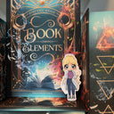 Das Produktbild zeigt ein Magnetlesezeichen mit einer blonden Frau, die einen knielangen, hellblauen Mantel und darunter ein rosafarbenes Hemd, eine blaue Hose und Chucks trägt. Das Lesezeichen lehnt am Buch "Book Elements". Gezeichnet ist das Lesezeichen im Anime-Stil.