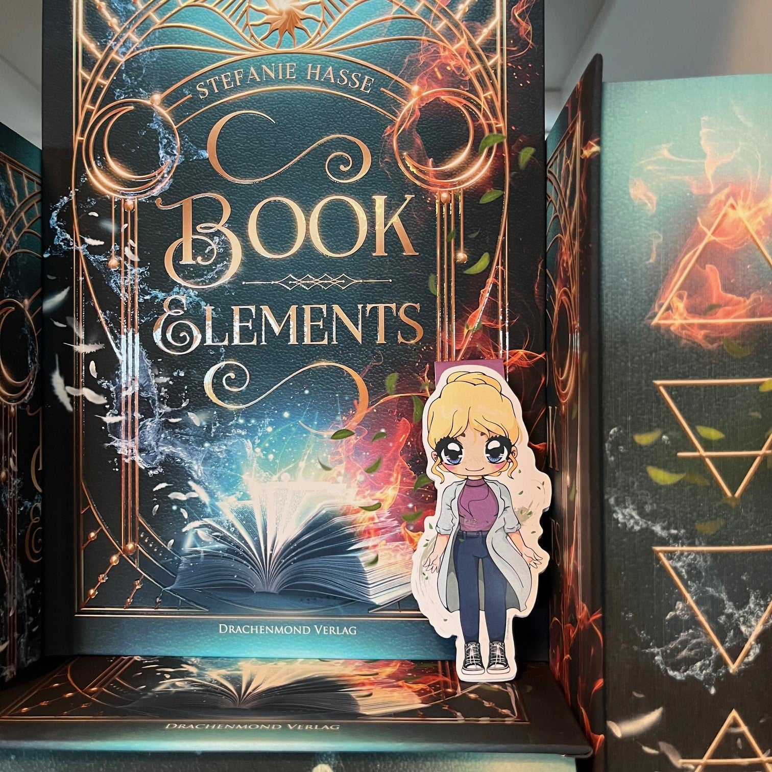 Das Produktbild zeigt ein Magnetlesezeichen mit einer blonden Frau, die einen knielangen, hellblauen Mantel und darunter ein rosafarbenes Hemd, eine blaue Hose und Chucks trägt. Das Lesezeichen lehnt am Buch 