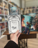 Das Bild zeigt die Charakterkarte und den Signiersticker zu dem Buch "Book Elements". Die Charakterkarte zeigt die Protagonistin Lin und den Feuerelementar Ric, die sich gegebüberstehen und einander in die Augen schauen. In Rics linker Hand loder eine Flamme, um Lin wirbelt eine Windhose. Der Signiersticker ist verziert mit dem Rahmen vom Buchcover. 