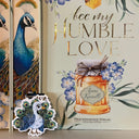 Das Produktbild zeigt ein Magnetlesezeichen mit einem Pfau. Oben links fliegt eine kleine Hummel.