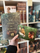 Das Bild zeigt, wie eine Hand das Buch "Es war einmal im Dunklen Wald" von Anne Danck und (davor) die Charakterkarte mit den beiden Hauptfiguren des Buches hält. 