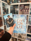 Das Bild zeigt das Buch "Love or Lie" und die dazugehörige Charakterkarte. Die Protagonisten Eyla und Dan stehen Arm in Arm in einer Winterlandschaft und schauen sich in die Augen.