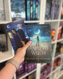 Auf dem Bild sieht man eine Hand, welche das Buch "Starlight Witch" als Softcover mit der dazu passenden Charakterkarte hält. Auf der Charakterkarte sind die Protagonistin und der Protagonist abgebildet.