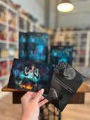 Auf dem Bild sieht man im Hintergrund das Buch "Seelenverflucht" und im Vordergrund eine Hand, welche die beiden Charakterkarten dazu hält. Auf der linken Karte sieht man die Protagonistin, welche vor einem Kessel steht. Aus dem Kessel kommt blauer Nebel. Auf der rechten Karte sieht man die Silhouette einer Person mit Hexenhut, einen Mond und die Silhouette eines Raben. Mittig steht ein Spruch.