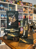 Das Bild zeigt einen Stapel von "Eine Krone aus Stroh und Gold". Das Cover ist dabei direkt auf den Betrachter gerichtet und der Farbschnitt sowie der Buchrücken bei den liegenden Büchern sichtbar.