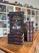 Das Bild zeigt einen Stapel von "Jack the Ripper's Sammlung der Herzen". Das Cover ist dabei direkt auf den Betrachter gerichtet und der Farbschnitt sowie der Buchrücken bei den liegenden Büchern sichtbar.