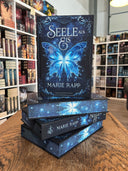 Das Bild zeigt einen Stapel von "Seele aus Eis". Das Cover ist dabei direkt auf den Betrachter gerichtet und der Farbschnitt sowie der Buchrücken bei den liegenden Büchern sichtbar.