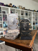 Das Bild zeigt zwei Stapel von "Das Vermächtnis der Grimms"; den Band 1 in Weiß und Band 2 in Schwarz. Das Cover ist dabei direkt auf den Betrachter gerichtet und der Farbschnitt sowie der Buchrücken bei den liegenden Büchern sichtbar.