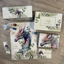 Das Bild zeigt eine Buchbox, ein Poster, die Danke-Karte, ein Lesezeichen und ein eingepacktes Buch. Alles ziert ein Drache in Lila- und Grüntönen, der von Eukalyptus-Blättern umgeben ist. 
Ein paar Süßigkeiten sind ebenfalls zu sehen. 