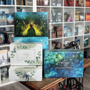 Das Bild zeigt vor den Bücherregalen im Drachennest unsere Drachenpost-Designs - die Märchenbox, die blaue Drachenschuppenbox und die weiße Box mit dem blau-violettem Drachen.