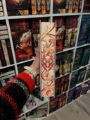Auf dem Bild sieht man vor Bücherregalen das Buch "Lilienfluch & Fuchsmagie" so gehalten, dass der Farbschnitt zu sehen ist. 