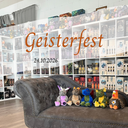 Auf dem Bild sieht man vier Plüschdrachen auf einem Sofa sitzen, das vor Bücherregalen steht. Darüber befindet sich der Schriftzug des Events samt Datum. 