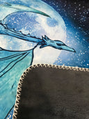 Das Produktbild zeigt einen Ausschnitt der Drachenmond-Decke. Man erkennt von der Vorderseite einen Teil des Drachen vor dem Mond am Sternenhimmel und von der Rückseite das graue Fleece. 