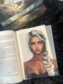Das Page Overlay zeigt das Porträt der weiblichen Hauptfigur des Buches "Asrai - Das Portal der Drachen". Elaja hat einen weißblonden, geflochtenen Zopf, der über die Schulter nach vorn fällt, und Tätowierungen im Dekolleté. 
