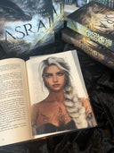Das Page Overlay zeigt das Porträt der weiblichen Hauptfigur des Buches "Asrai - Das Portal der Drachen". Elaja hat einen weißblonden, geflochtenen Zopf, der über die Schulter nach vorn fällt, und Tätowierungen im Dekolleté. 