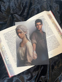 Das Page Overlay zeigt die Hauptfiguren aus "Asrai - Das Portal der Drachen". Elaja, mit weißblondem Zopf und heller Kleidung, befindet sich links vorn, Ian mit dunklen Haaren und dunklem Hemd rechts dahinter. Er schaut in ihre Richtung, sie hat sich abgewendet. Hinter ihrem Rücken verschränken sich ihre Hände jedoch. 