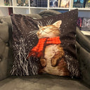 Das Produktbild zeigt ein schwarzes Kissen auf einer grauen Couch. Auf dem Kissen ist eine braune Katze mit geschlossenen Augen abgebildet, die einen roten Schal trägt und auf ihren Hinterbeinen sitzt. 