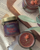 Das Produktbild zeigt unsere Drachenkerze "Königin der Sterne" aus verschiedenen Perspektiven. In der geöffneten Kerze sieht man neben dem Docht einen kleinen Fuchs  auf braunem Wachs mit goldenem Glitter. Eine Kerze liegt auf der Seite, um das Label zu zeigen. Mittig steht der Titel auf dem bräunlich-violetten Untergrund. An den Rändern hängen Äste mit grünen Blättern. Unter dem goldenen Deckel hängt ein Band mit einem Fuchs-Anhänger.