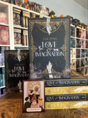 Das Bild zeigt einige Exemplare des Buches "Love & Imagination" von Lin Rina. Sie sind so gestapelt, dass man nicht nur den Rücken und das Front-Cover sieht, sondern auch den Farbschnitt. Davor steht eine von der Autorin gezeichnete Tarotkarte - "Die Hierophantin". 