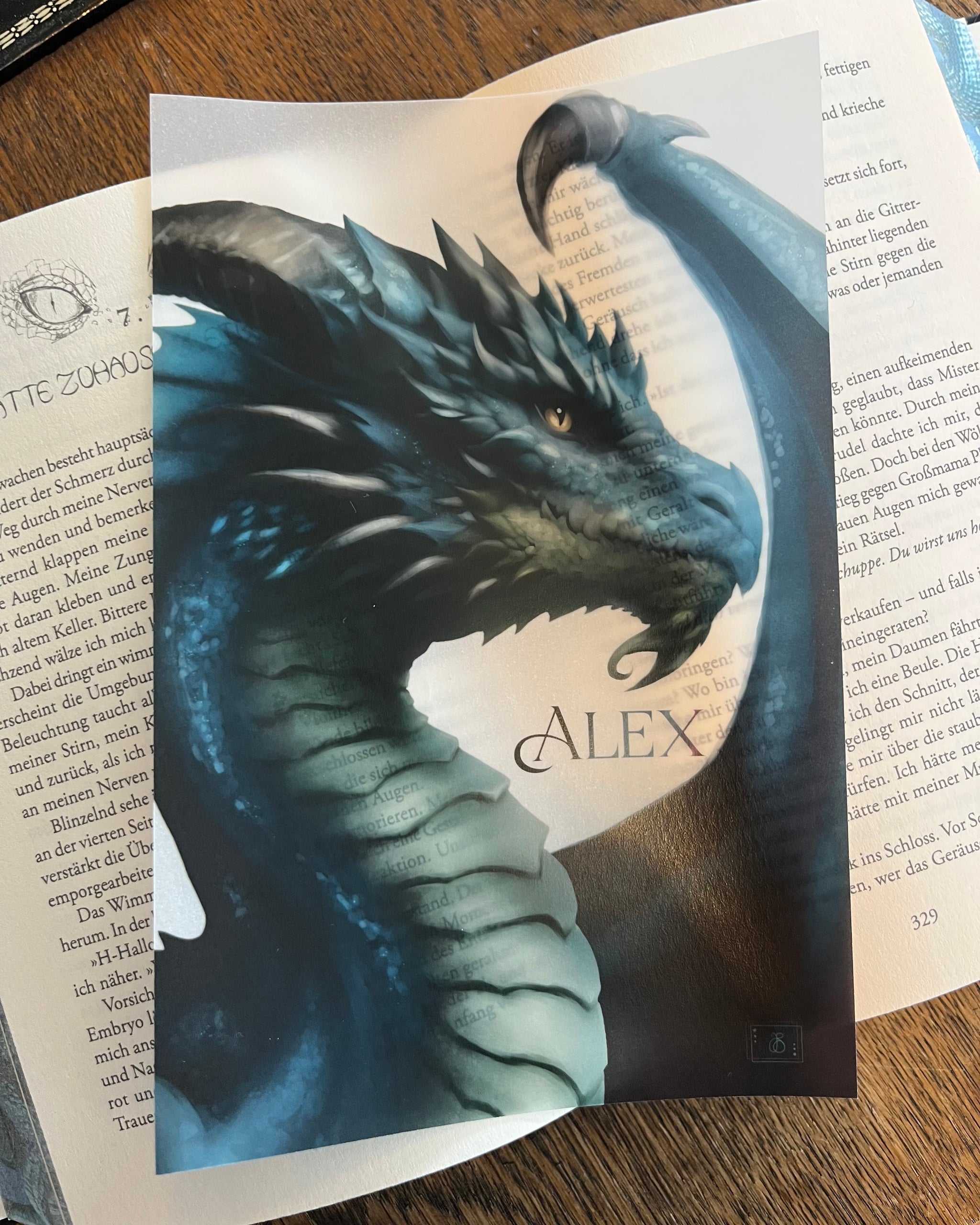 Das Page Overlay zeigt das Profil eines blauen Drachen. Das Page Overlay liegt auf einem aufgeschlagenen Buch, so dass man die Buchstaben durch das Papier schimmern sieht.