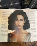 Das Page Overlay zeigt das Porträt der weiblichen Hauptfigur des Buches "Der dunkle Kuss der Sterne". Canda hat kinnlanges, lockiges, dunkles Haar. Sie trägt ein helles Oberteil. In ihrem Dekolleté sieht man grünblaue Symbole auf die Haut gezeichnet. 