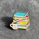 Das Produktbild zeigt einen Bücherstapel-Pin, vor dem ein Kaffeebecher mit der Aufschrift "sorry, i'm booked" steht. Die Farben der Bücher sind Hellblau, Rot und Gelb. Die Tasse ist weiß. Die Umrandung und die Schrift auf der Tasse sind golden.