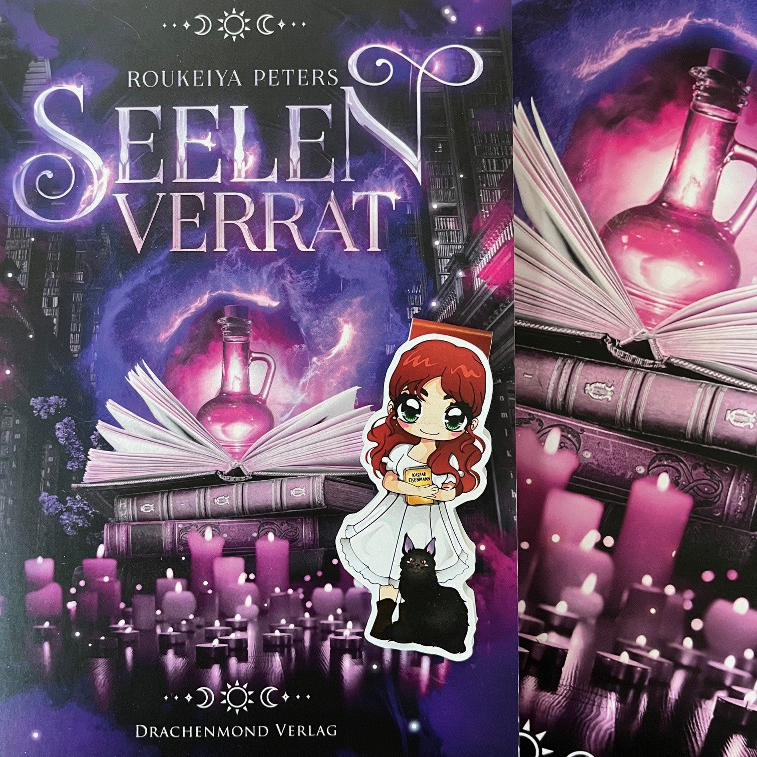 Das Produktbild zeigt ein Magnetlesezeichen mit einer rothaarigen Frau in einem weißen Kleid. In ihren verschränkten Armen hält sie ein Buch und vor ihr sitzt eine scharze Katze. Im Hintergrund ist das Cover von dem Buch 