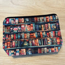 Das Produktbild zeigt ein Täschchen, auf dem ein gemaltes Bücherregal mit bunten Büchern und einigen, wenigen Deko-Elementen abgebildet ist. 