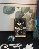 Auf dem Bild sieht man einen Pin, der eine Tarotkarte "The Reader" nachempfunden ist. 