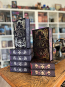 Das Bild zeigt die beiden "Warrior & Peace"-Bücher von Stella Tack. Das erste Cover ist dunkellila. Der Titel befindet sich in silbernem Spotlack mittig darauf. Umgeben ist er von verschiedenen Elementen, ebenfalls in silbernem Spotlack, die mit der griechischen Antike verbunden werden: Säulen, Schlangen, Helme, Lorbeeren, eine Amphore und weitere Verzierungen. Das zweite Cover zeigt die gleichen Motive, ist aber dunkelrot mit Goldfolie.
