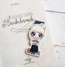 Das Produktbild zeigt ein Magnetlesezeichen im Anime-Stil, das in dem aufgeschlagenen Buch "Staubchronik" liegt. Das Lesezeichen zeigt die Figur Animant aus dem Buch. Sie trägt eine Gelbe Bluse und einen schwarzen langen Rock. Vor ihrer Brust hält sie drei Bücher. Rechts und links neben ihr, liegen Bücherstapel auf dem Boden.