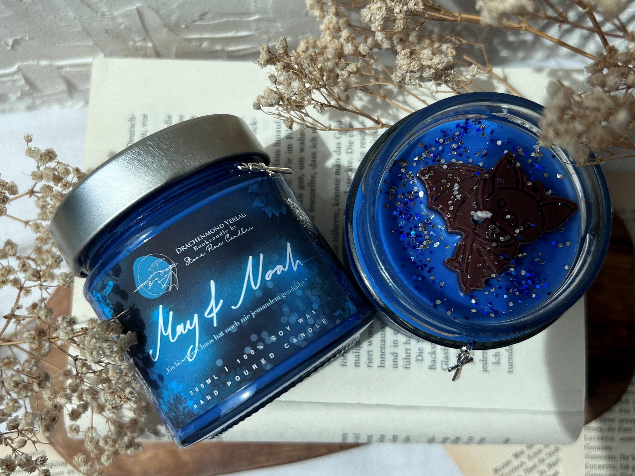 Das Produktbild zeigt die Kerze zur Chaos-Trilogie aus verschiedenen Perspektiven. Unter dem silbernen Deckel hängt ein kleiner Anch-Anhänger an einem blauen Band. Auf dem blauen Label steht mittig in weißer Schrift 