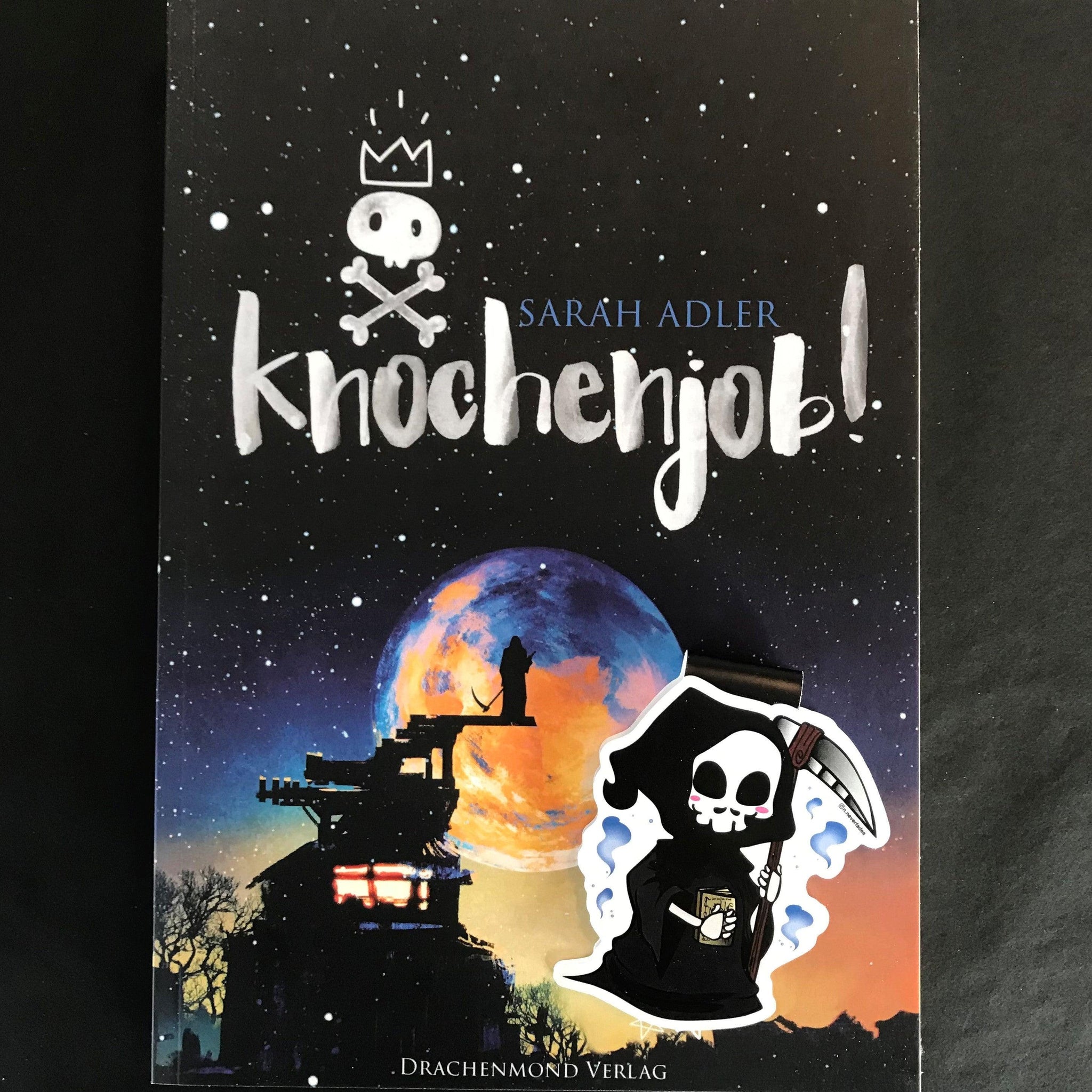 Das Produktbild zeigt ein Magnetlesezeichen mit einem Sensenmann, der eine Sense in der linken Hand und ein goldenes Buch in der rechten Hand hält. Im Hintergrund ist das dazugehörige Buch 