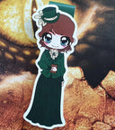 Das Produktbild zeigt ein Magnetlesezeichen mit einer brünetten Frau in einem grünen viktorianischen Outfit mit passendem grünen Hütchen. Vor ihrem Bauch hält sie ein braunes Buch.