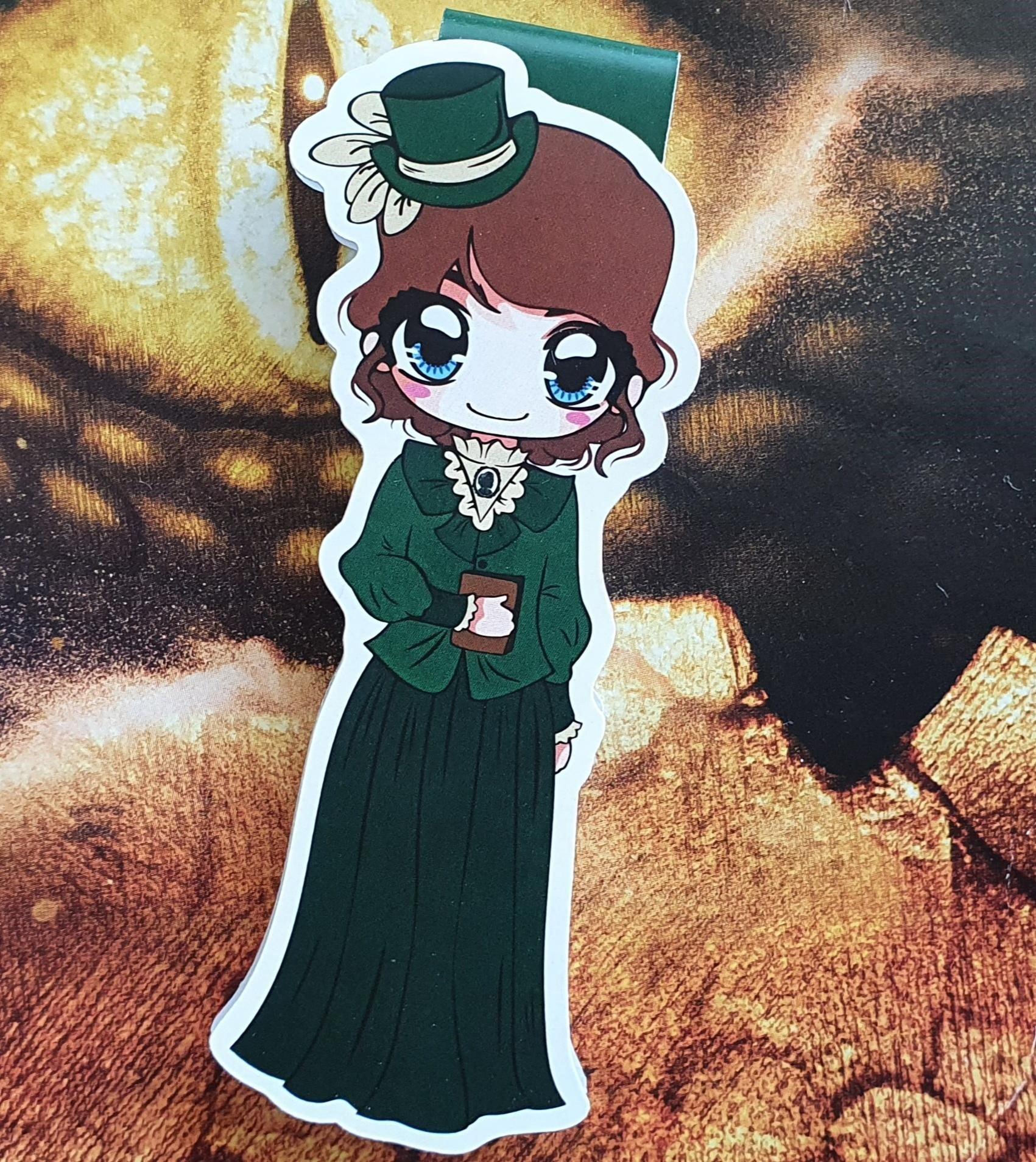 Das Produktbild zeigt ein Magnetlesezeichen mit einer brünetten Frau in einem grünen viktorianischen Outfit mit passendem grünen Hütchen. Vor ihrem Bauch hält sie ein braunes Buch.