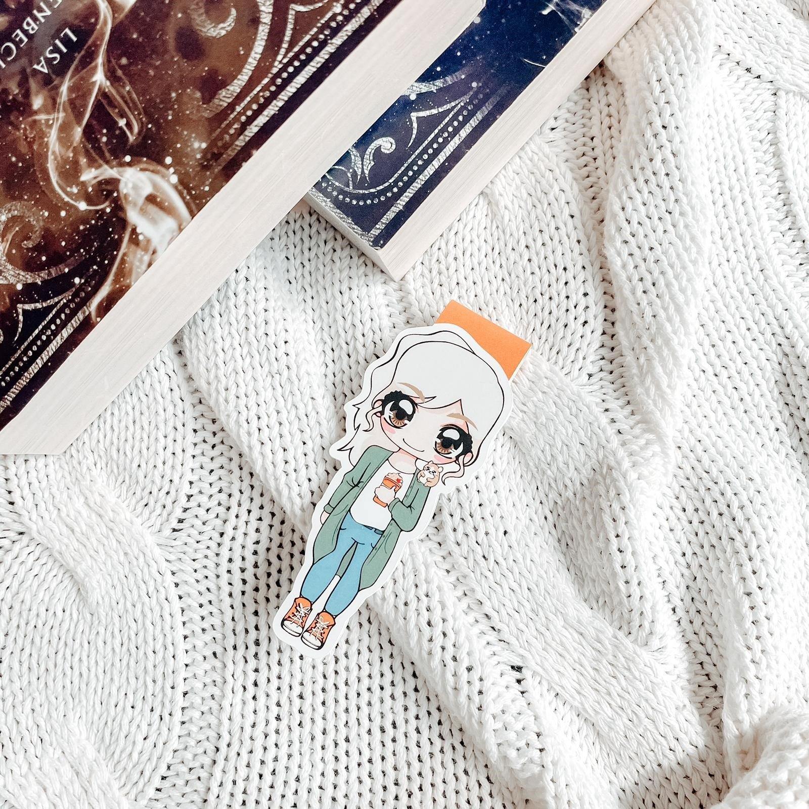 Das Produktbild zeigt ein Magnetlesezeichen mit einer blonden Frau. Sie trägt ein weißes Shirt, darüber einen langen grünen Cardigan, eine blaue Hose und orange-weiße Schuhe. In ihrer linken Hand hält Sie einen orangenen Becher und auf ihrer Schulter sitzt ein braun-weißer Hamster. Gezeichnet ist das Lesezeichen im Anime-Stil.