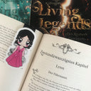 Das Produktbild zeigt ein Magnetlesezeichen mit der weiblichen Hauptfigur Lynn aus der Trilogie "Living Legends". Die schwarzhaarige Frau trägt ein pinkes Kleid und in ihrer rechten Hand hält sie einen gebogenen Dolch. Gezeichnet ist das Lesezeichen im Anime-Stil .