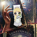 Das Produktbild zeigt ein Magnetlesezeichen mit einer blonden Frau in einem langen Dienstmädchenkleid. Auf ihrer Schulter sitzt ein kleiner grüner Drache, auf ihrem Kopf ein hellgrauer Drache. 